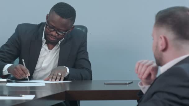 Hombre de negocios negro firma un contrato y le da papeles a un socio — Vídeo de stock