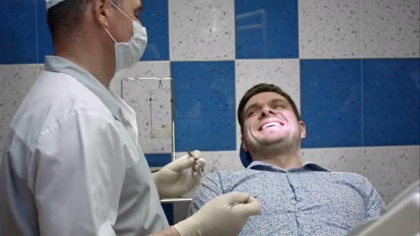 Αρσενικό οδοντίατρος εξετάζει τα δόντια του πελάτη του αρσενικό — Αρχείο Βίντεο