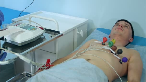 Νοσοκόμα με εξοπλισμό ΗΚΓ κάνοντας τεστ καρδιοκαρδιογράφημα σε αρσενικό ασθενή σε νοσοκομειακή κλινική — Αρχείο Βίντεο