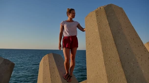 Sonriente hermosa chica de pie sobre bloques de hormigón en frente del mar — Vídeos de Stock