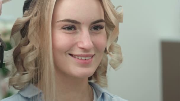 Відображення усміхненої молодої жінки з світлим волоссям у дзеркалі салону, стилізованому під волосся — стокове відео