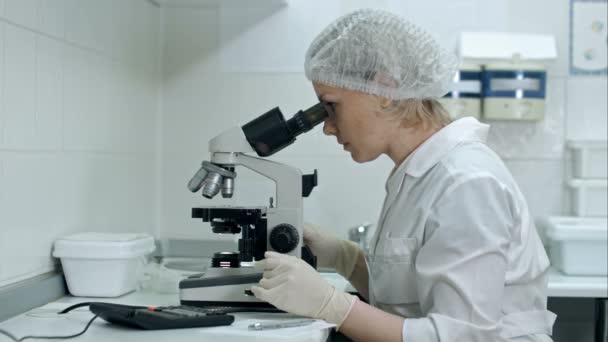 Ученый, работающий с микроскопом, вычисляющий и делающий заметки в лаборатории — стоковое видео