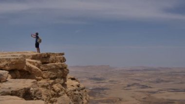 Uçurumun kenarında duran ve çölde yaptığı telefon panoramik fotoğraf çekici genç adam
