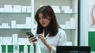 Genç kadın eczacı manifatura iletileri istimal hareket eden telefon, gülümseyen ve onun erkek colleauge konuşuyor