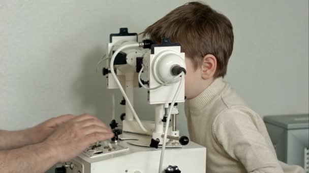 Vieux médecin masculin examine les yeux du garçon à travers la lampe à fente — Video