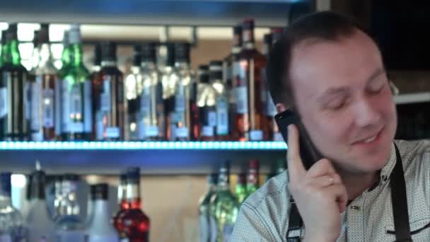 Glad bartendern i förkläde uppmanar smartphone på bar — Stockvideo