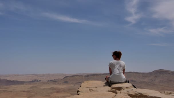 Νεαρή γυναίκα κάθεται στην άκρη των βράχων και βλέπουν στην έρημο — Αρχείο Βίντεο