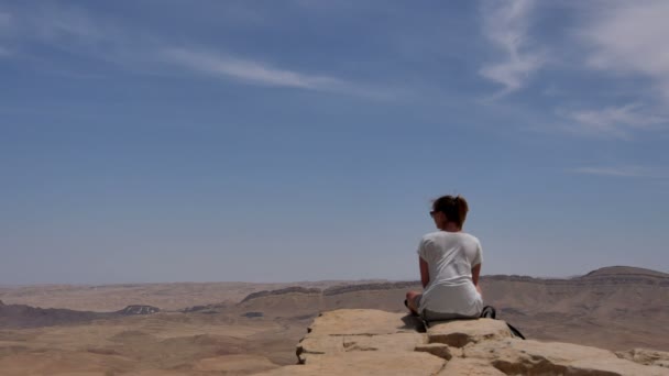 Young woman sitting on cliffs edge and looking at the desert — Stock Video