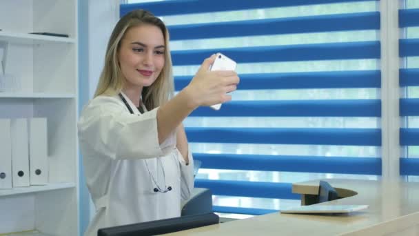 Enfermera sonriente tomando selfies con su teléfono detrás de la recepción — Vídeo de stock