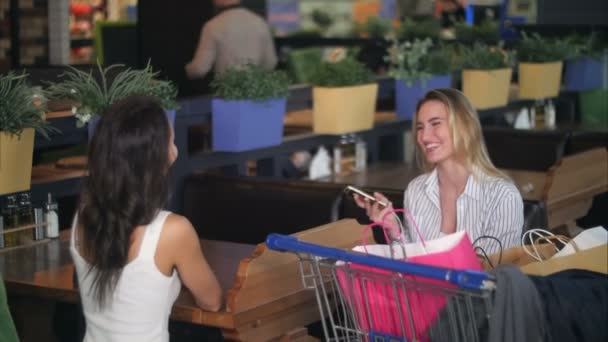 Freunde, die nach dem Einkaufen in einem Café im Einkaufszentrum eine Pause einlegen und Smartphones benutzen — Stockvideo