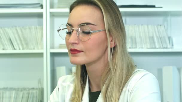 Attrayant jeune femme médecin dans des lunettes assis au bureau dans le bureau — Video