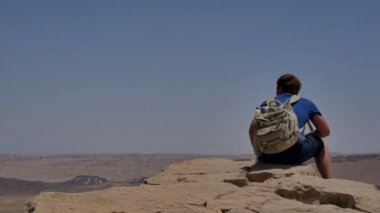 Uçurum kenarında oturan ve çöl seyir sırt çantası ile genç adam