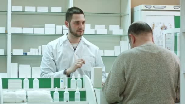 Молодой фармацевт дает препарат старшему клиенту и принимает оплату в долларах в аптеке — стоковое видео
