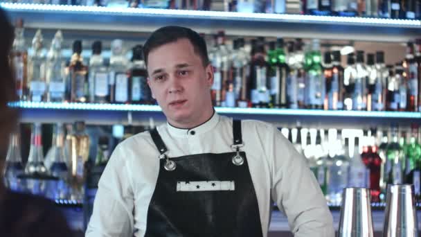 Веселый молодой бармен улыбается и разговаривает с клиентом в баре — стоковое видео