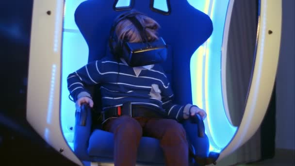 Pequeño niño experimentando realidad virtual sentado en silla móvil interactiva — Vídeos de Stock