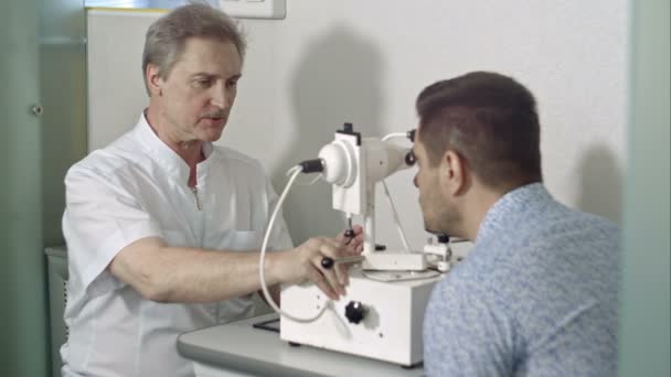 Пожилая женщина-офтальмолог и мужчина-клиент проверяют зрение в клинике — стоковое видео