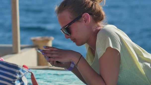 Mladá žena v sluneční brýle s smartphone na pláži — Stock video