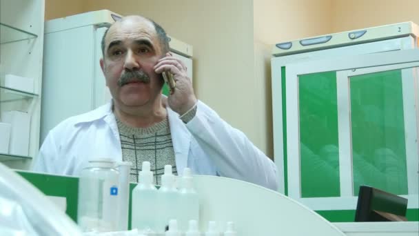 Smiling farmacéutico senior en el teléfono en la farmacia — Vídeo de stock