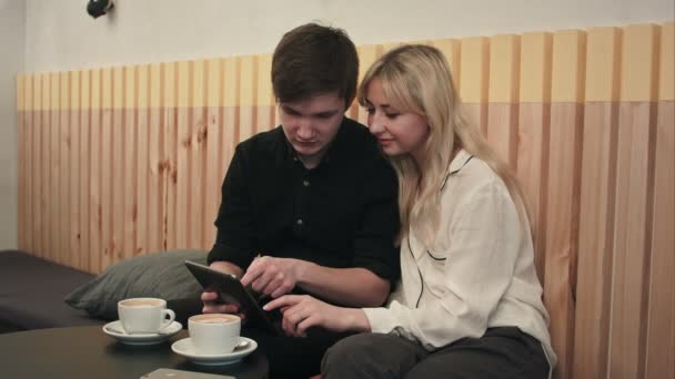 Ungt par på ett café, dricka kaffe och använda digitala surfplatta — Stockvideo