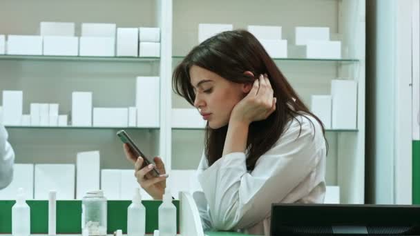 Verveeld vrouwelijke apotheker mobiele telefoon gebruiken bij apotheek — Stockvideo