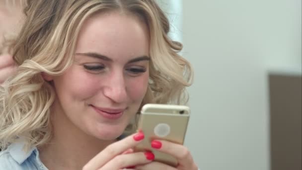 Vrouw met haar styling in salon tijdens het surfen op het internet op haar mobiele telefoon, glimlachend — Stockvideo