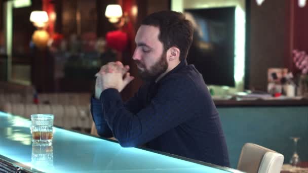 Веселий привабливий молодий чоловік п'є в барі і дивиться на камеру посміхаючись — стокове відео