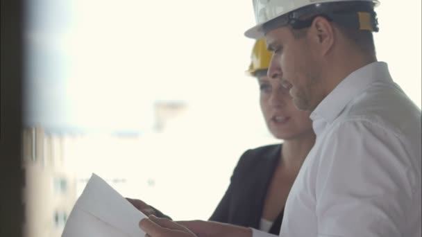 Hombre de negocios pensativo y mujer de negocios mirando el plan de proyecto juntos mientras trabajan en el sitio de las construcciones — Vídeos de Stock