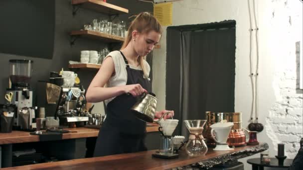 Young female barista in trendy modern cafe coffee shop pours boiling water over coffee grounds making a pour over drip coffee — Stock Video