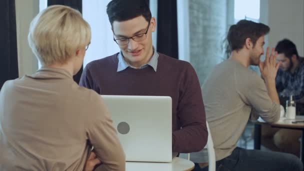 Deux jeunes gens d'affaires utilisant un ordinateur portable dans le hall du bureau moderne — Video