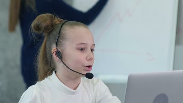 Cute little girl in headset sitting at table with laptop and having video conferance — Stock Video