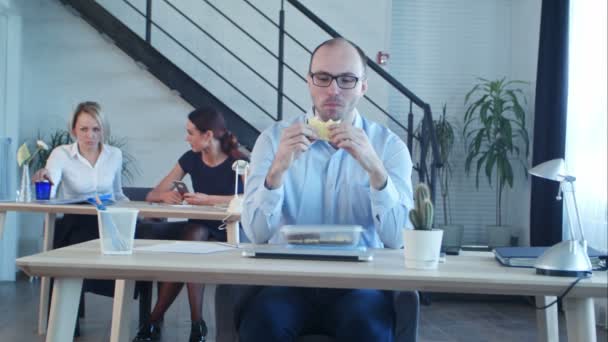 Молодой бизнесмен сидит с бутербродом в офисе — стоковое видео
