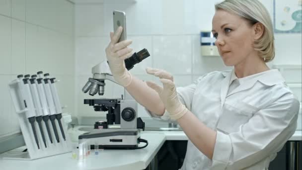 Female lab doctor with a smartphone taking selfie — Stock Video