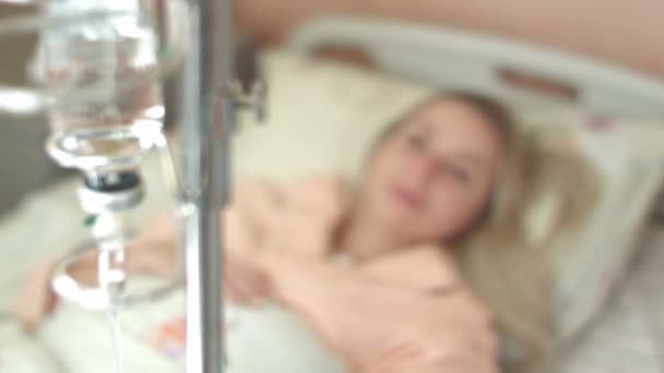 Jonge vrouw kijkt naar infusie fles op de stand in het ziekenhuis — Stockvideo