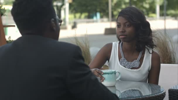 Μαύρο κορίτσι με κρατώντας ένα φλιτζάνι καφέ, μιλάμε για η afro Αμερικανός συνάδελφός της, κάθεται έξω από το καφενείο — Αρχείο Βίντεο