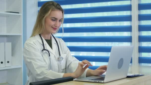 Усміхнена медсестра друкує на ноутбуці і робить нотатки на рецепції — стокове відео