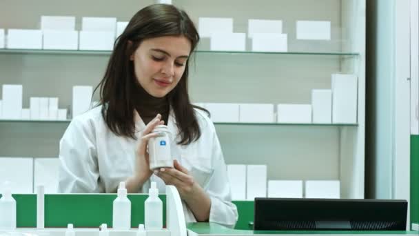 性格开朗的年轻女子药剂师与一瓶站在药房药店看看相机的药物 — 图库视频影像