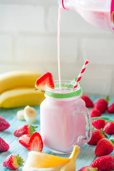 Freschi agricoltori biologici fragola e banana frullato versando dalla bottiglia in un barattolo di vetro — Foto Stock