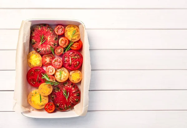 Paj med tomater, olivolja, parmesanost och rosmarin på pergament papper i keramiska skålen. Vit trä bord bakgrund, kopiera utrymme, ovanifrån. — Stockfoto