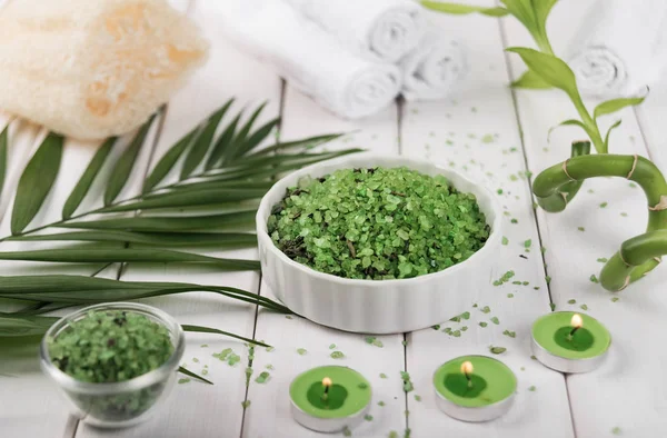 Spa. Sal de espirulina de hierbas verdes en tazón de cerámica blanca, toallas de spa, velas y bambú — Foto de Stock