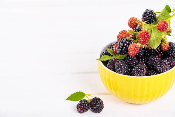 Ripe blackberries with leaves in a yellow modern bowl on a wooden board on a light background — Stock Photo, Image