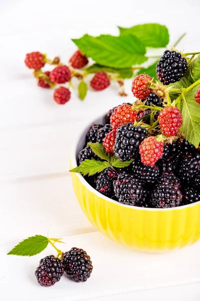 Ripe blackberries with leaves in a yellow modern bowl on a wooden board on a light background — Stock Photo, Image