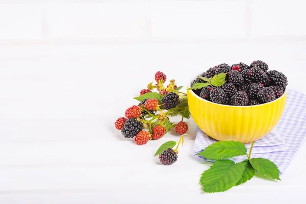 Ripe blackberries with leaves in a yellow modern bowl on a wooden board on a light background — Stock Photo, Image