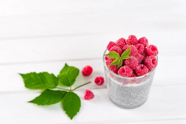 Food and drink, healthy eating and dieting concept. Homemade white chia pudding with fresh berries and green leaves for breakfast on a light kitchen table. Glass with raspberry. Copy space. — Stock Photo, Image