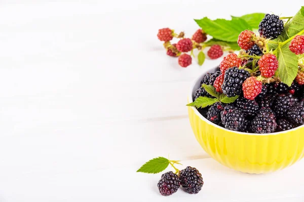 Ripe blackberries with leaves in a yellow modern bowl on a wooden board on a light background — Stock Photo, Image