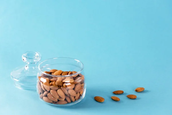 Almonds in glass bowl on blue background. Copy space — Stock Photo, Image