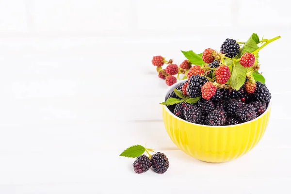 Ripe blackberries with leaves in a yellow modern bowl on a wooden board on a light background — Stock Photo, Image
