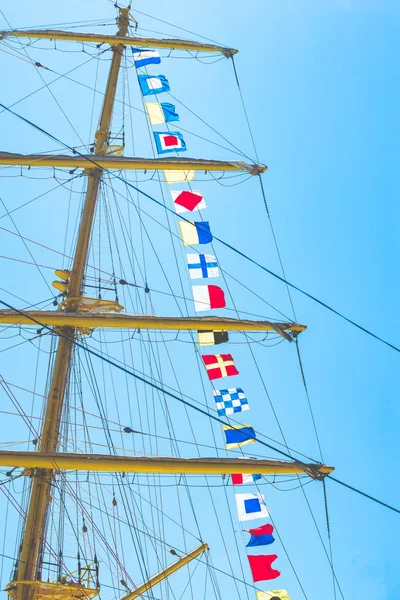 Разноцветные парусные флаги, развевающиеся на ветру от линий мачты парусника, подсвеченные ярко-голубым небом на солнце — стоковое фото