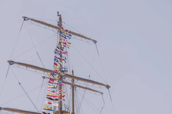 Colorful nautical sailing flags flying in the wind from the lines of a sailboat mast backlit in bright blue sky by the cloudy stormy day. Retro toned. — Stock Photo, Image