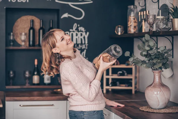 Фото юной смеющейся дамы, стоящей на современной кухне с бутылкой печенья в руке. Концепция питания . — стоковое фото