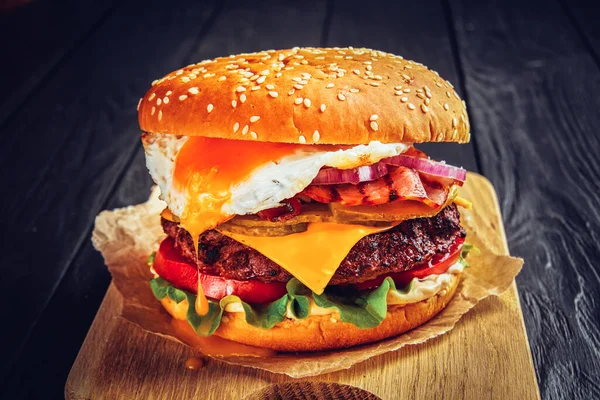 Beef burger with melted cheese and bacon and egg on wooden background